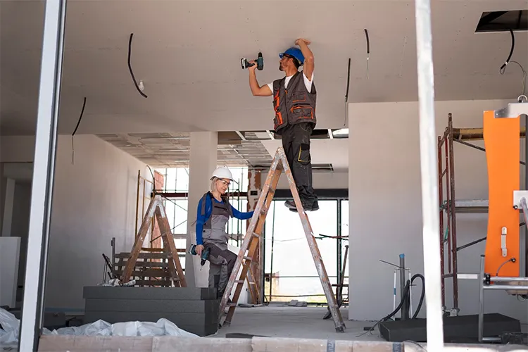 Two builders expertly installing plasterboard on a ceiling.